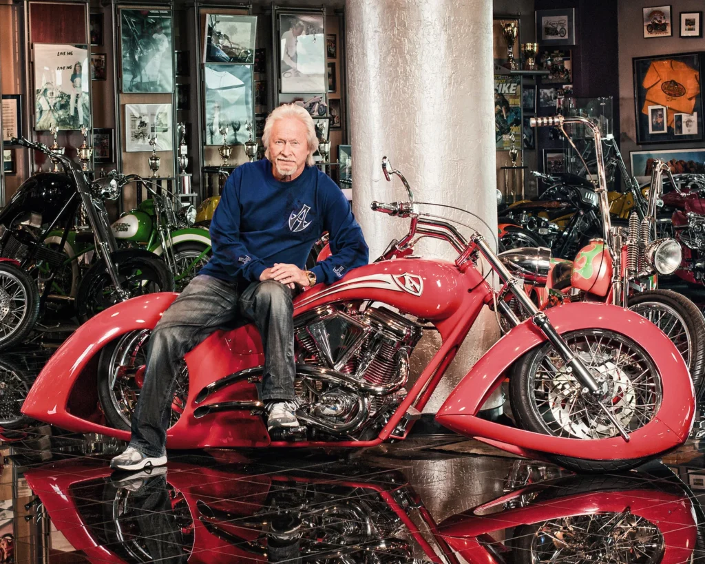 Arlen Ness sentado en una moto custom roja en su exhibición